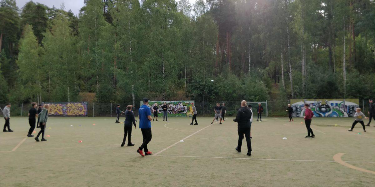 Junioreita ulkokentällä, taustalla kesäinen koivumetsä.