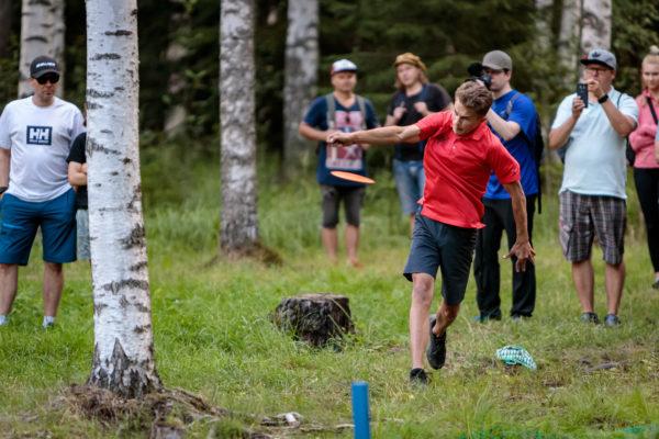 Niklas Anttila heittää Tampereen frisbeegolfkeskuksessa koivujen lomassa.