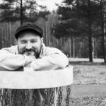 Petri Anttiroiko pitää molempia käsiään frisbeegolfkorin päällä ja nojaa leukaansa koriin, hymyillen.