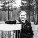 Johanna Parviainen seisoo frisbeegolfkorin takana käsi korin päällä ja hymyilee.